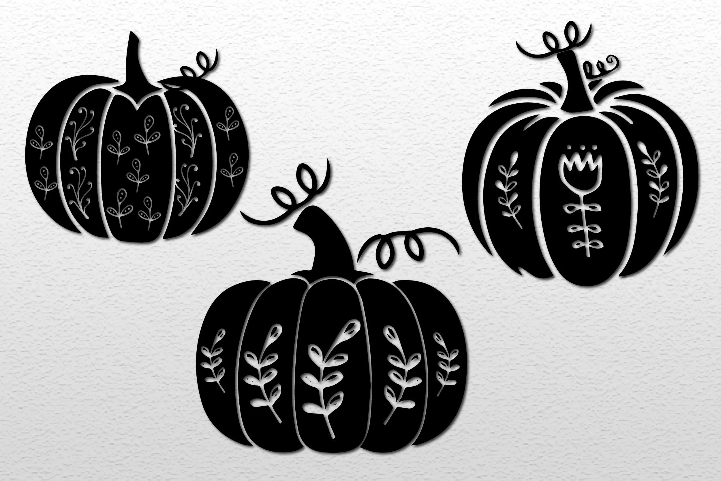 Floral Halloween Pumpkin SVG showing three black pumpkin silhouettes with white negative-space floral and foliate carving patterns on a textured white background.